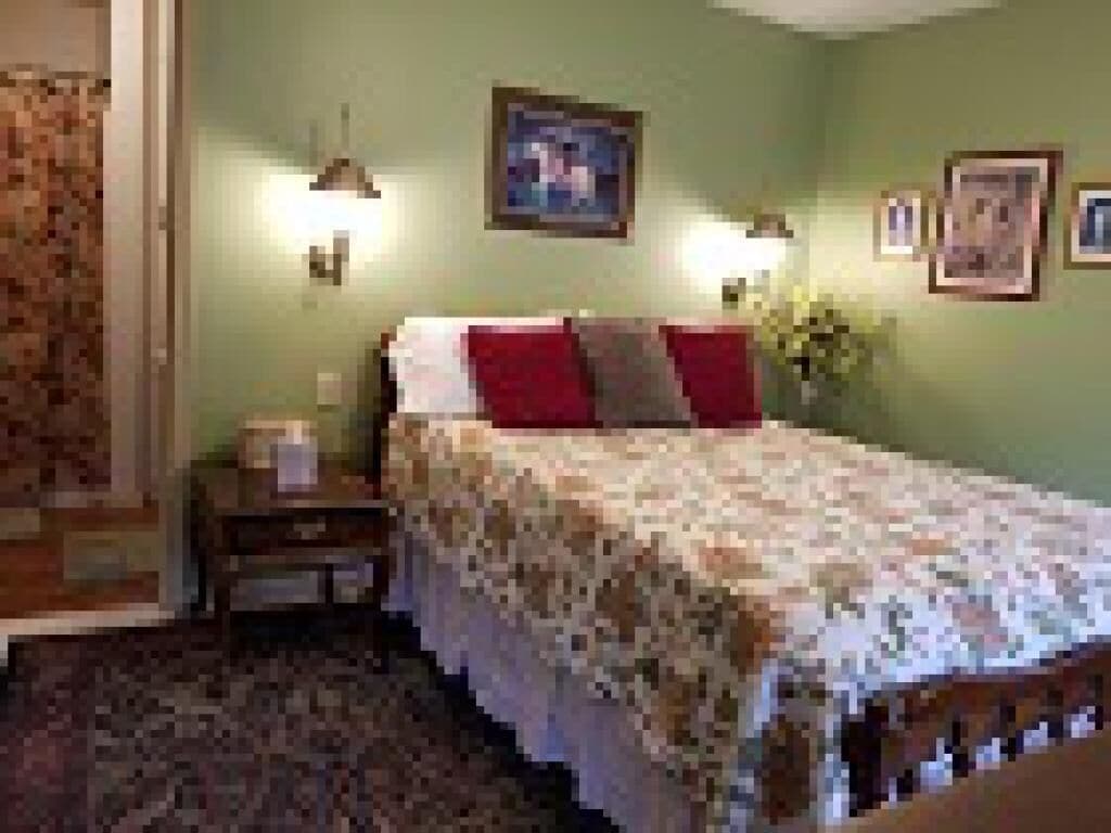 A bedroom with a bed, nightstand, wall-mounted lamps, and framed pictures.