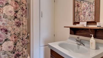 Un bany amb cortina de bany de flors, un lavabo blanc amb dosificador de sabó i un moble de tocador de fusta.