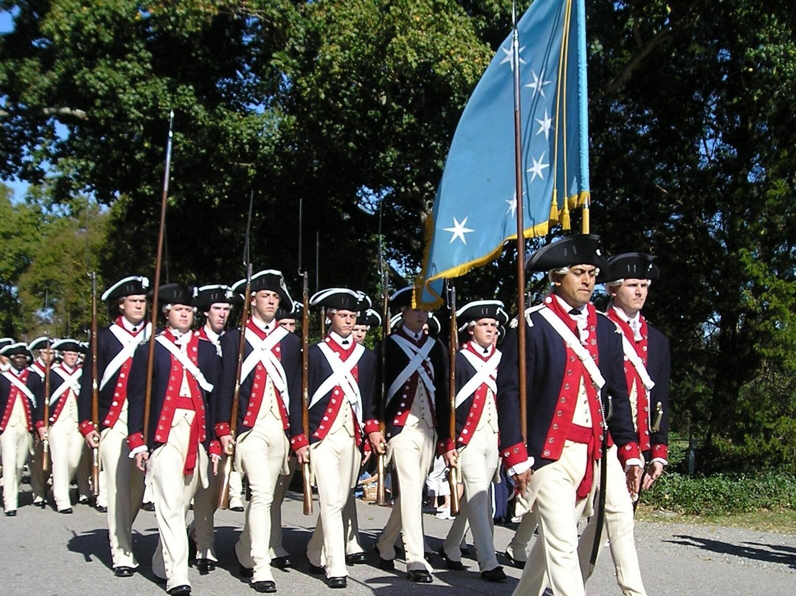A group of people in historical uniforms marching with a flag.
