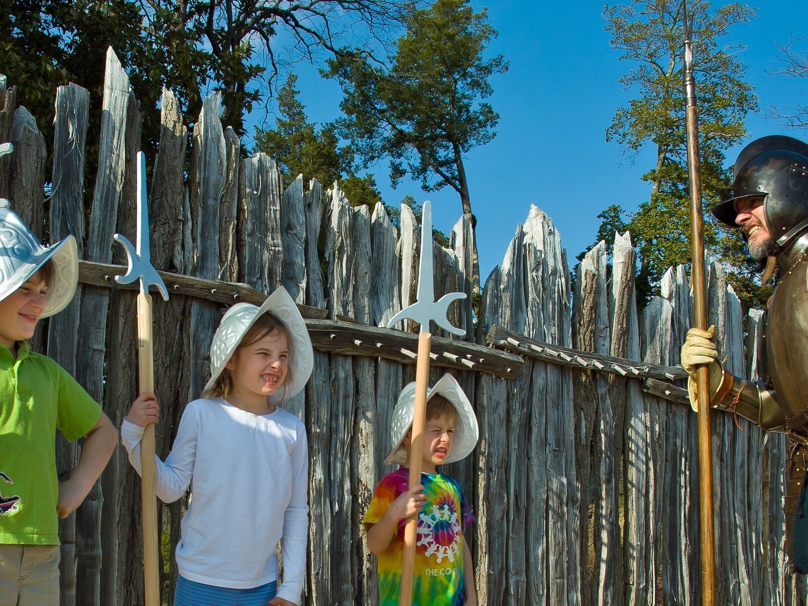 A group of people in medieval costumes with swords and shields, standing in front of a wooden fence.
