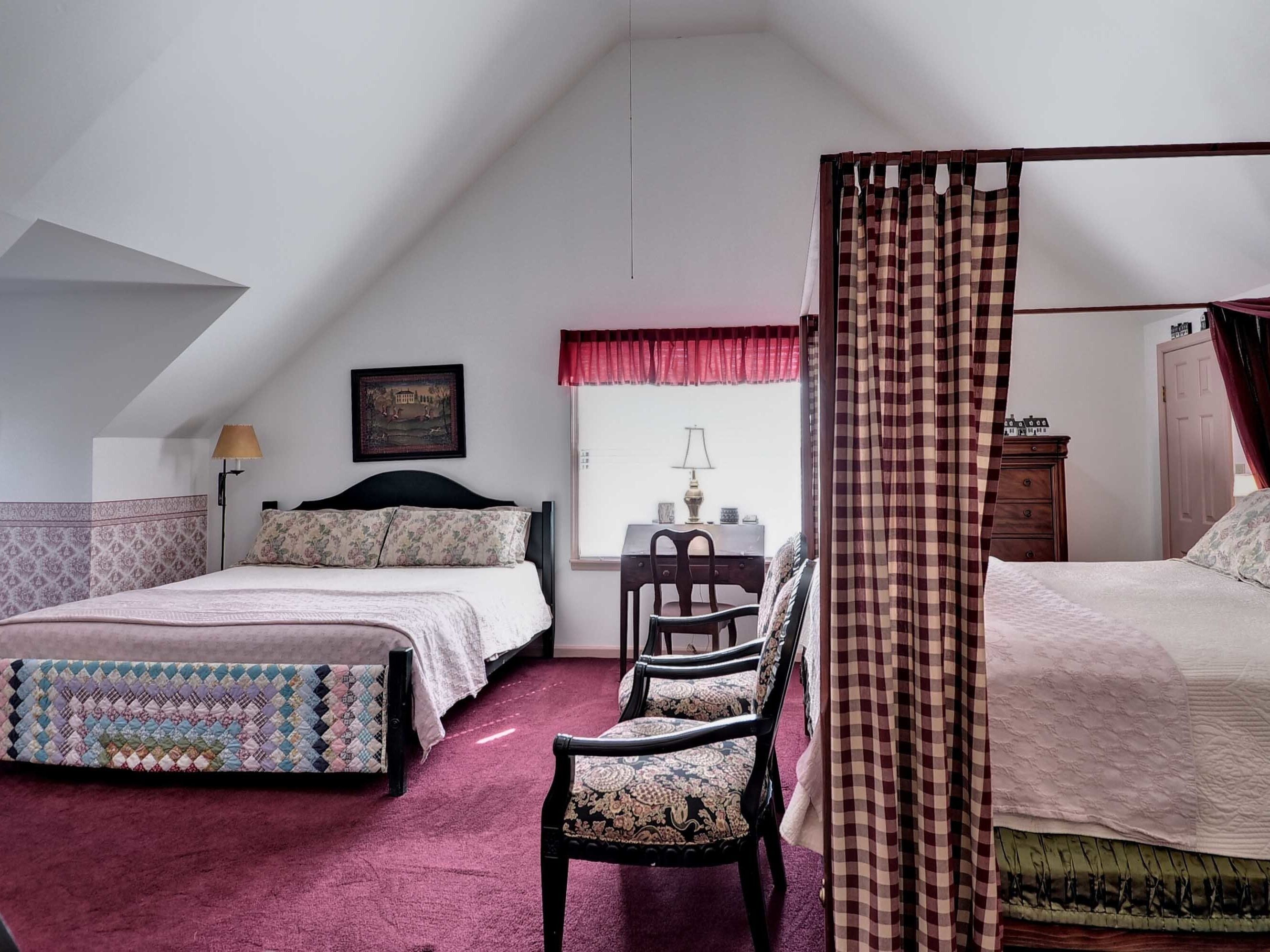 A bedroom with two beds, a chair, a desk, and a window with curtains.