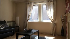 A living room with a sofa, a coffee table, a lamp, and a window with curtains. - Majesty Weavers Loan (Dundee)