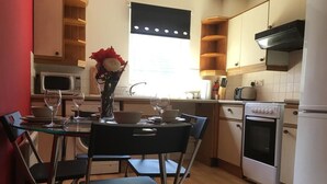 A compact kitchen with a dining table, chairs, a microwave, a stove, and a refrigerator. - Majesty Weavers Loan (Dundee)