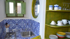 A kitchen with blue patterned tiles, a gas stove, a sink, and a green window with open shutters. - Appartamento Zeus (Lipari)