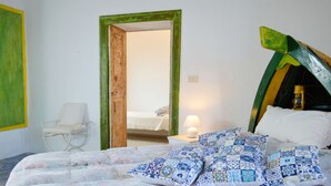 A bedroom with a bed, a nightstand, a chair, and a door leading to another room. - Appartamento Zeus (Lipari)