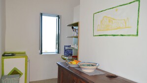 A room with a wooden dresser, a window, a shelf with dishes, and a wall with a yellow drawing. - Appartamento Zeus (Lipari)