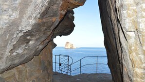 A rocky coastal view with a metal railing and a large rock formation in the distance. - Appartamento Zeus (Lipari)