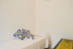 A small, neatly made bed with a white quilt and a blue and yellow patterned pillow. - Appartamento Zeus (Lipari)