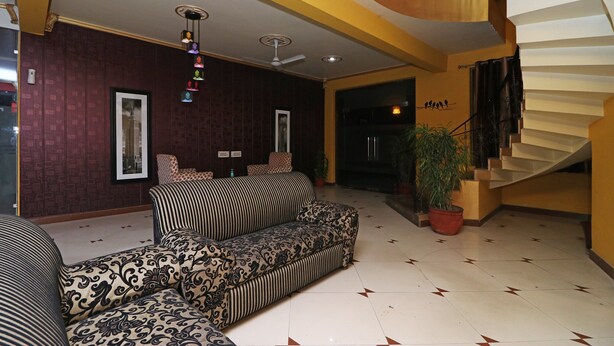 A modern living area with patterned sofas, a staircase, and a potted plant. - OYO 6590 Hotel Amaraa (Gurugram)
