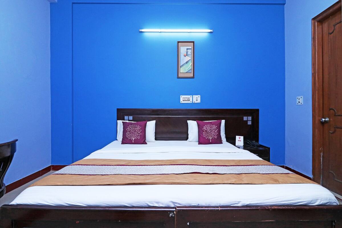 A hotel room with a large bed, a nightstand, a framed picture on the wall, and a wooden door.