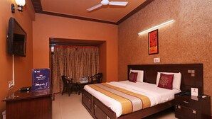 A hotel room with a bed, bedside tables, a desk, a chair, a ceiling fan, a wall-mounted TV, and a framed picture. - OYO 6590 Hotel Amaraa (Gurugram)