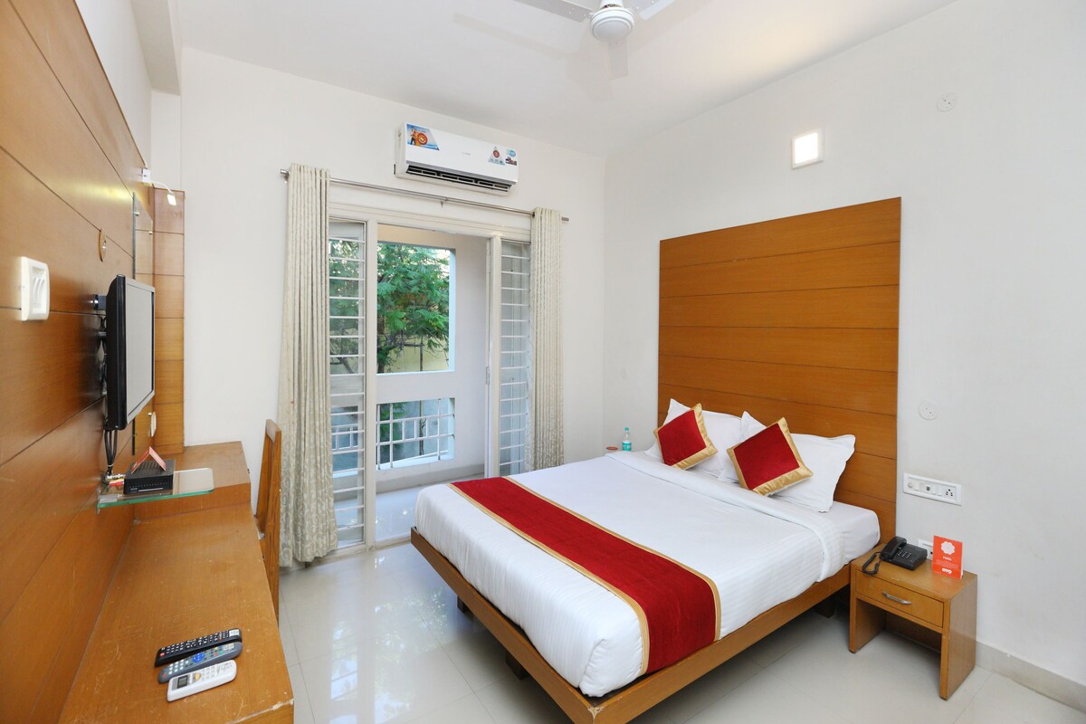 A hotel room with a bed, bedside table, TV, and an air conditioning unit.