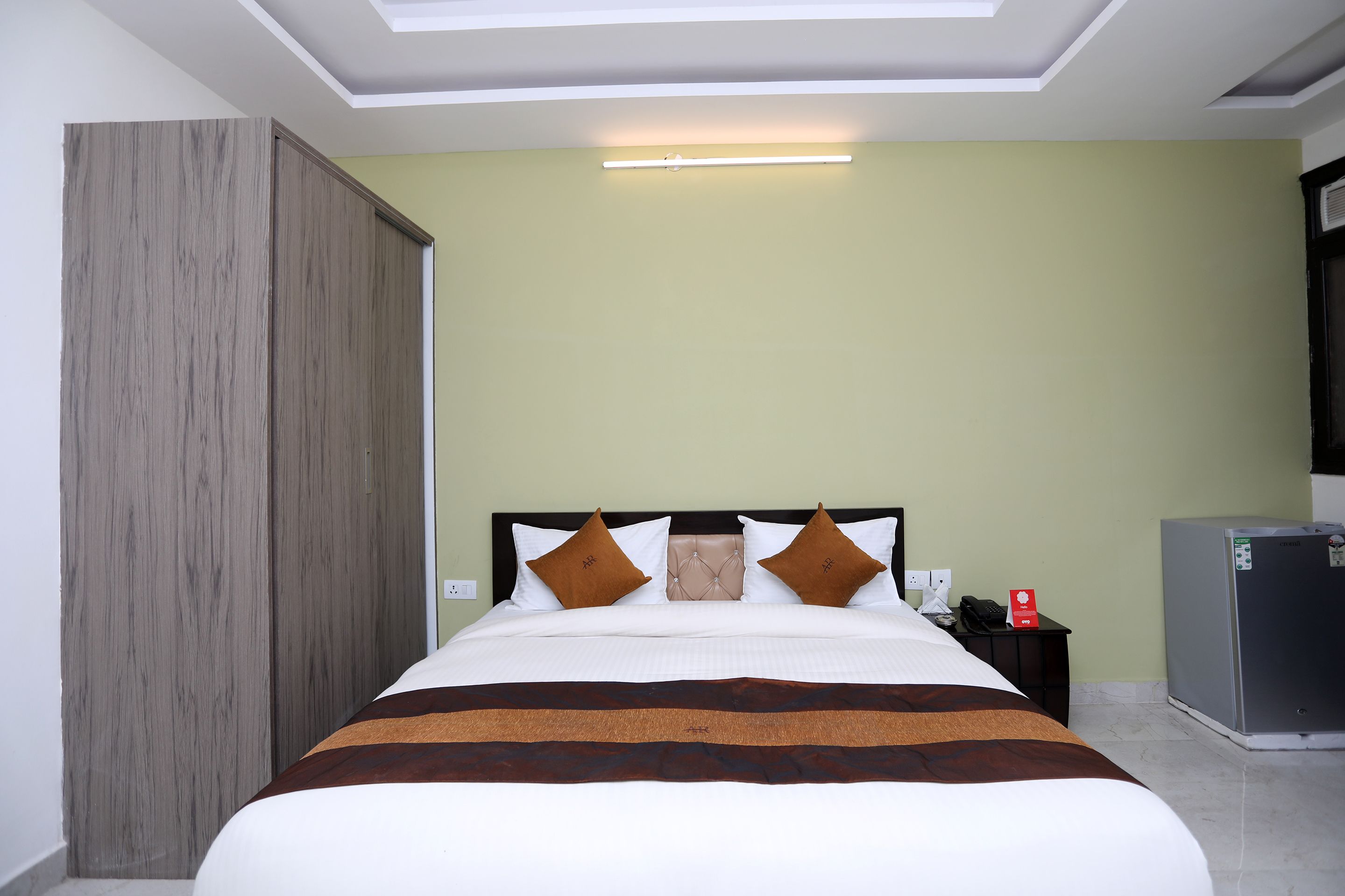A hotel room with a bed, a nightstand, a refrigerator, and a wardrobe.