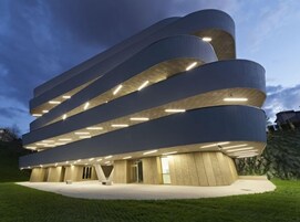 Un edificio moderno con una arquitectura curva distintiva y varios niveles iluminados.