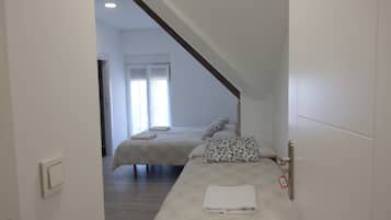 A hotel room with two beds, a wooden ceiling beam, and a window with curtains.
