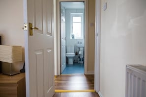 Un couloir menant à une salle de bain équipée de toilettes, d’un lavabo et d’étagères de rangement.