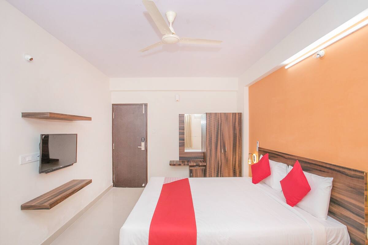 A hotel room with a bed, a TV, a ceiling fan, and a wooden headboard.