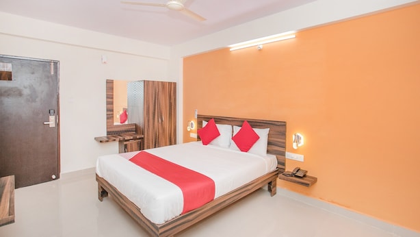 A hotel room with a wooden bed, a red throw, and a nightstand with a phone. - OYO 10475 PMR Hotel (Bengaluru)