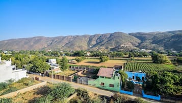 A rural landscape with a blue building, green fields, and mountains in the background.