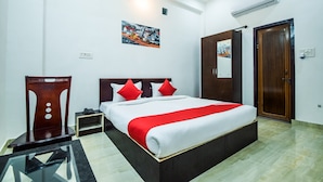 Een hotelkamer met een groot bed, een houten nachtkastje, een glazen tafel, een houten stoel en een schilderij aan de muur.