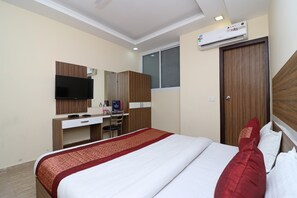 A hotel room with a bed, a desk with a chair, a TV, and an air conditioning unit. - OYO 10795 Hotel RS Residency (New Delhi)