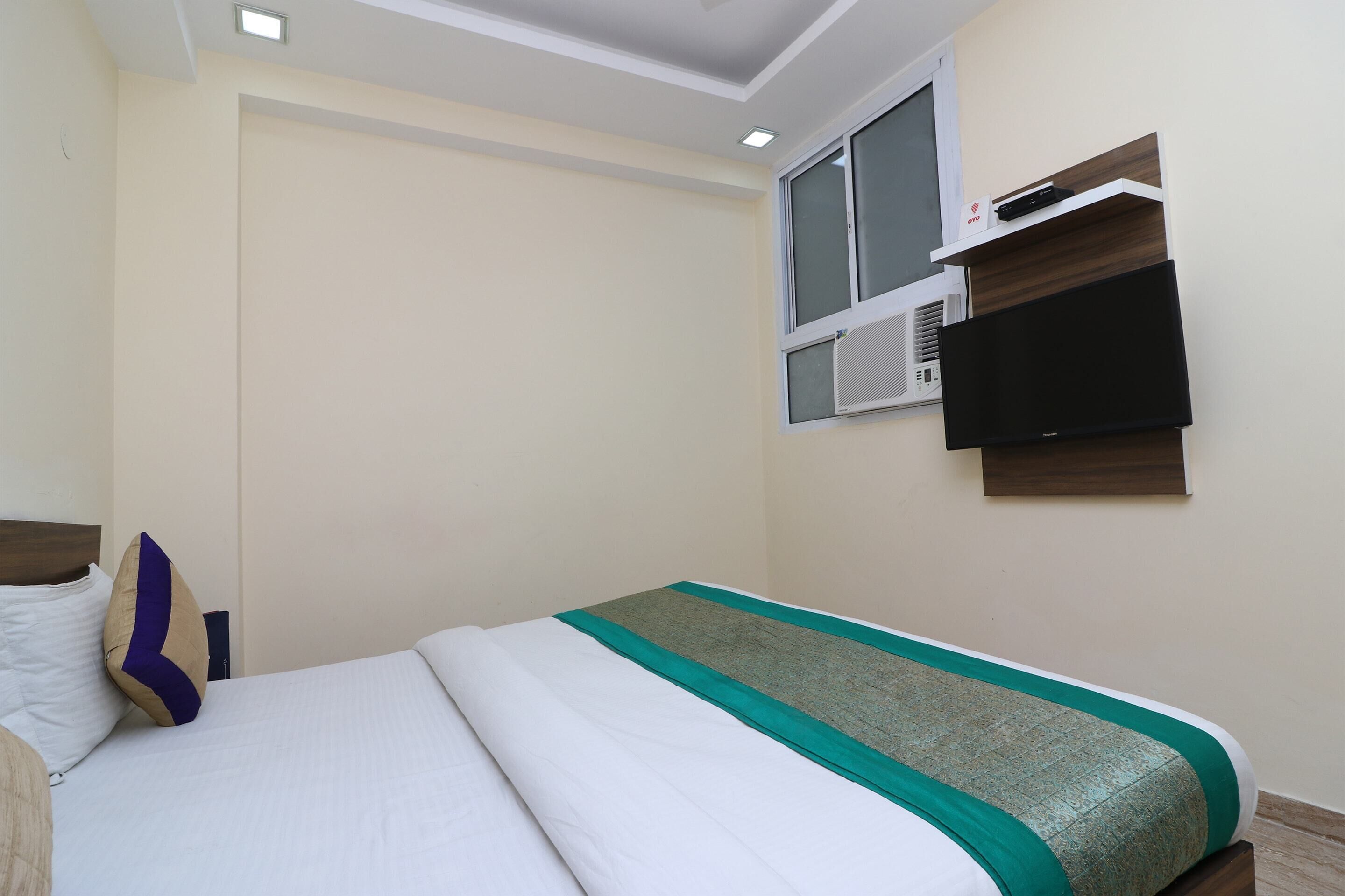 Habitación de hotel con cama, televisor de pantalla plana en la pared y ventana con unidad de aire acondicionado.