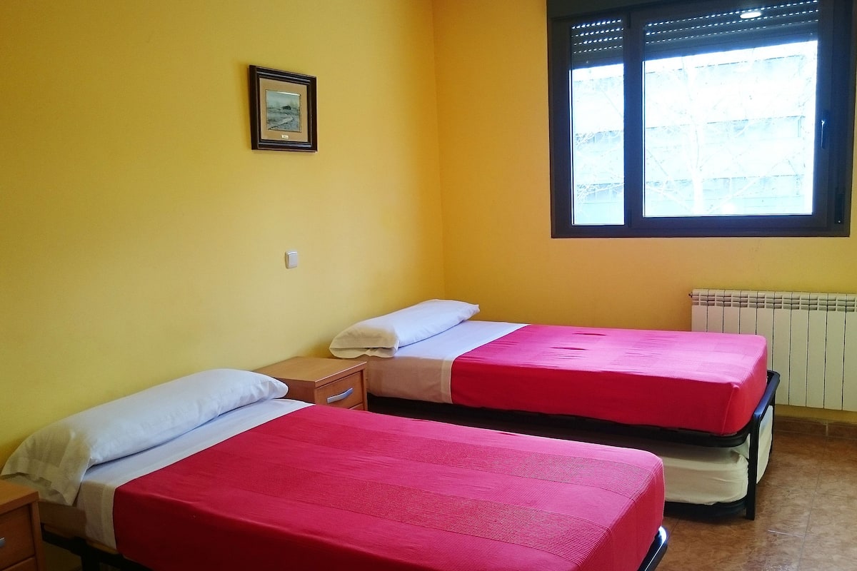 A room with two beds, a window, and a radiator.
