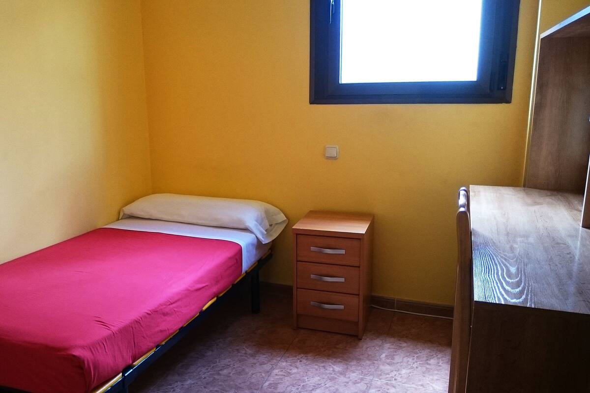 A small, single-bed room with a wooden dresser and a window.