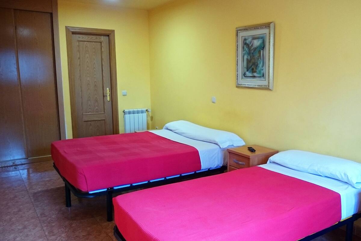 A room with two beds, each with a red bedspread and white pillows, a wooden nightstand with a phone, and a painting on the wall.