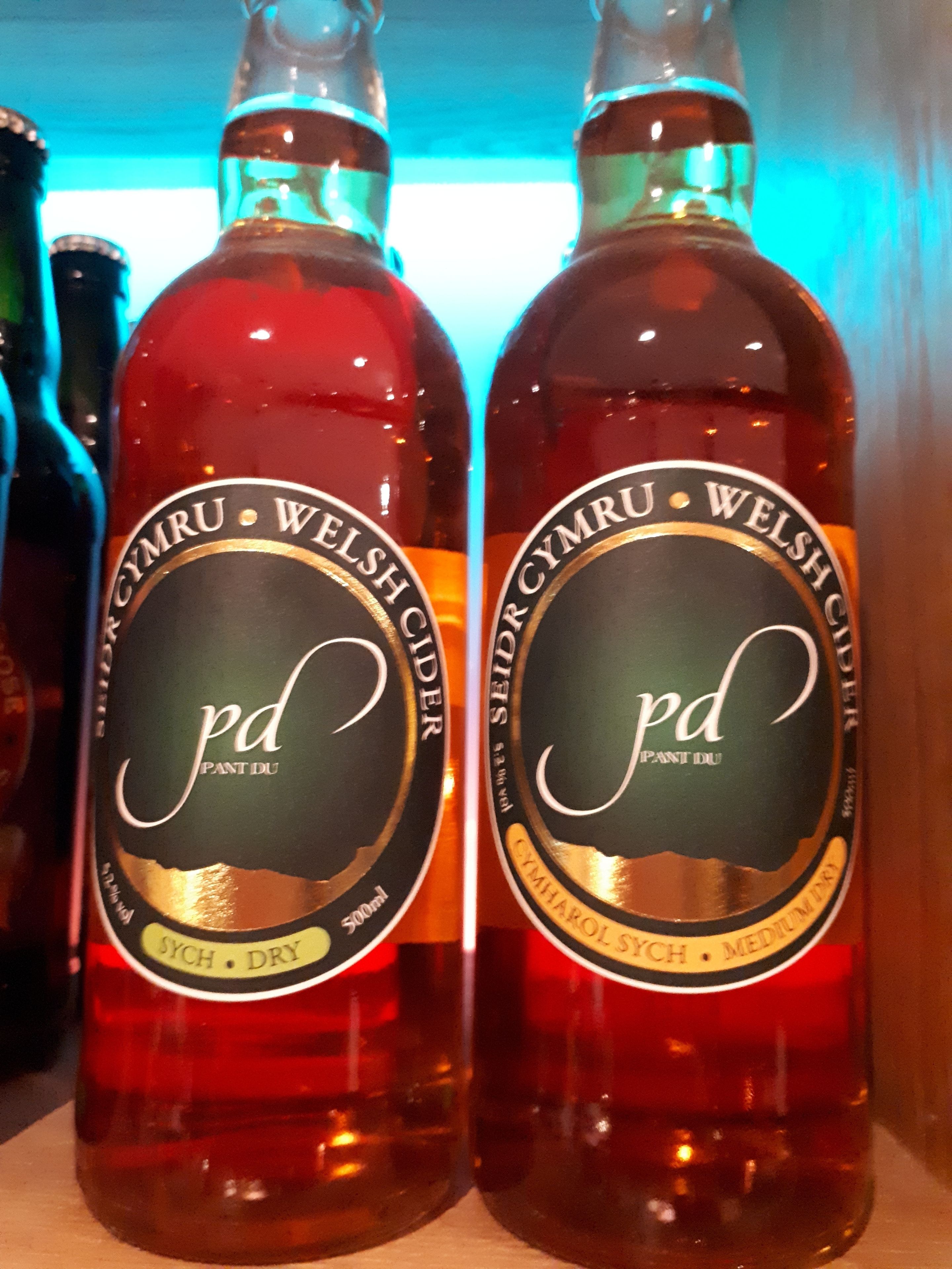 Two bottles of 'Cymharol Sych' medium dry cider with 'Cymru Welsh' branding, each labeled as 500ml.