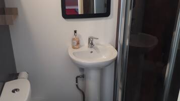 Un baño con inodoro blanco, lavamanos con pedestal, espejo y cabina de ducha con mampara de vidrio.