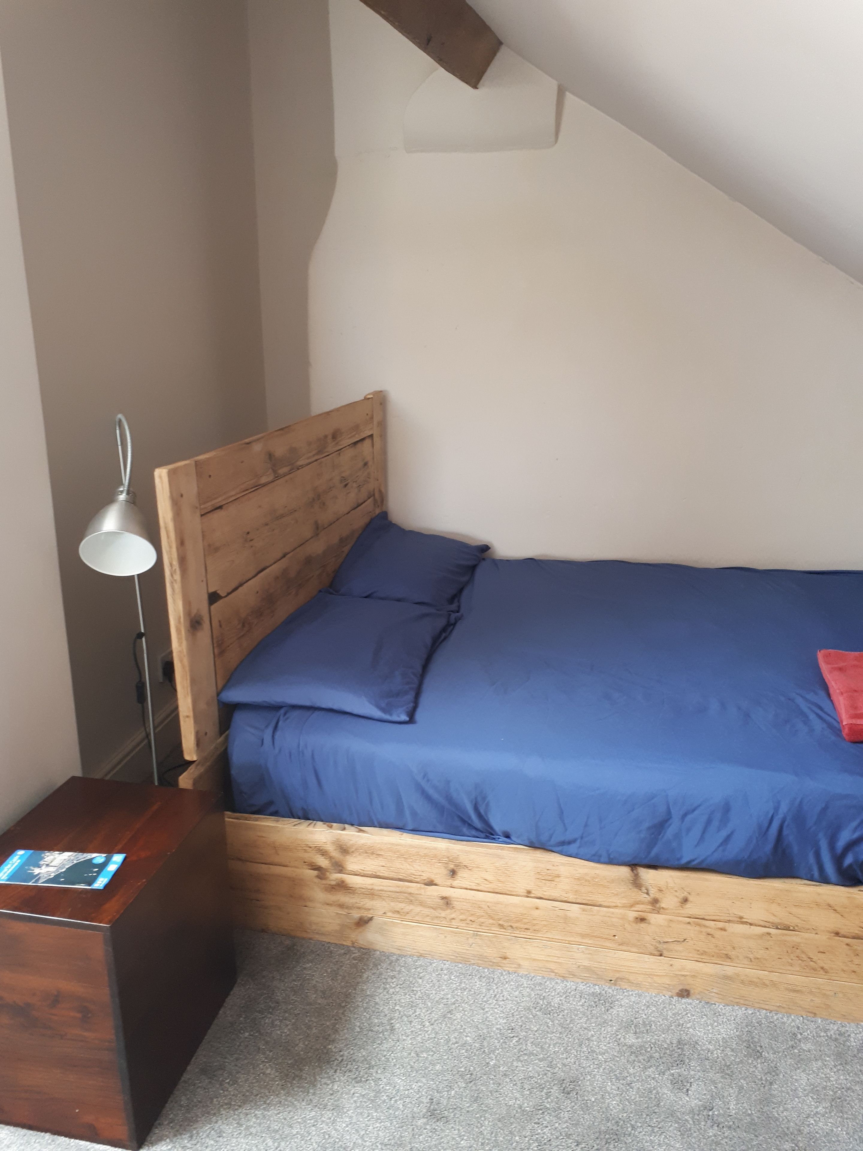 A small, cozy room with a wooden bed, a nightstand, and a lamp.