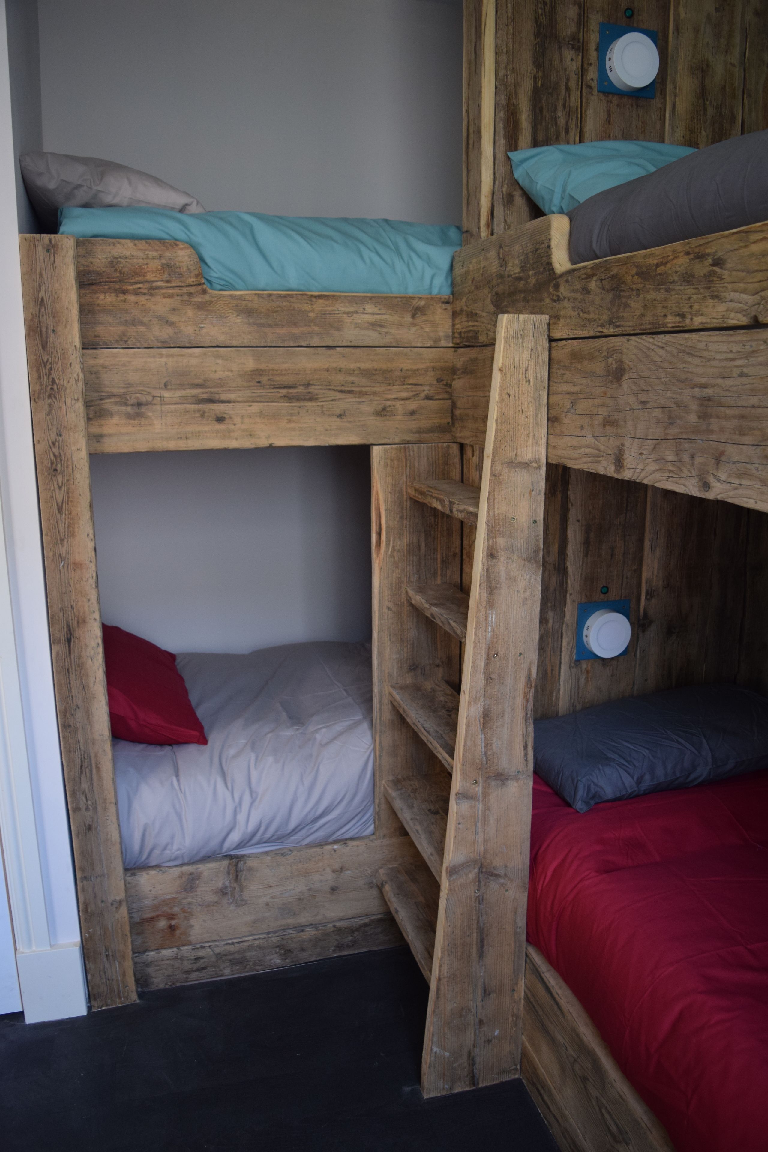 A bunk bed with a wooden frame, a lower bunk with a red pillow, and a top bunk with a teal pillow.