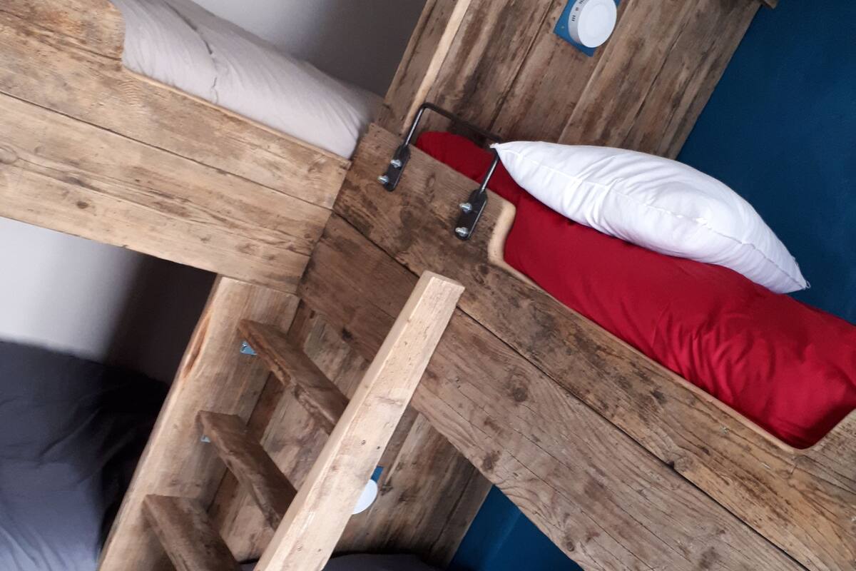 Un lit superposé avec une structure en bois, un matelas bleu et un oreiller rouge.
