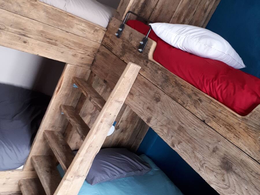 A bunk bed with a wooden frame, a blue mattress, and a red pillow.