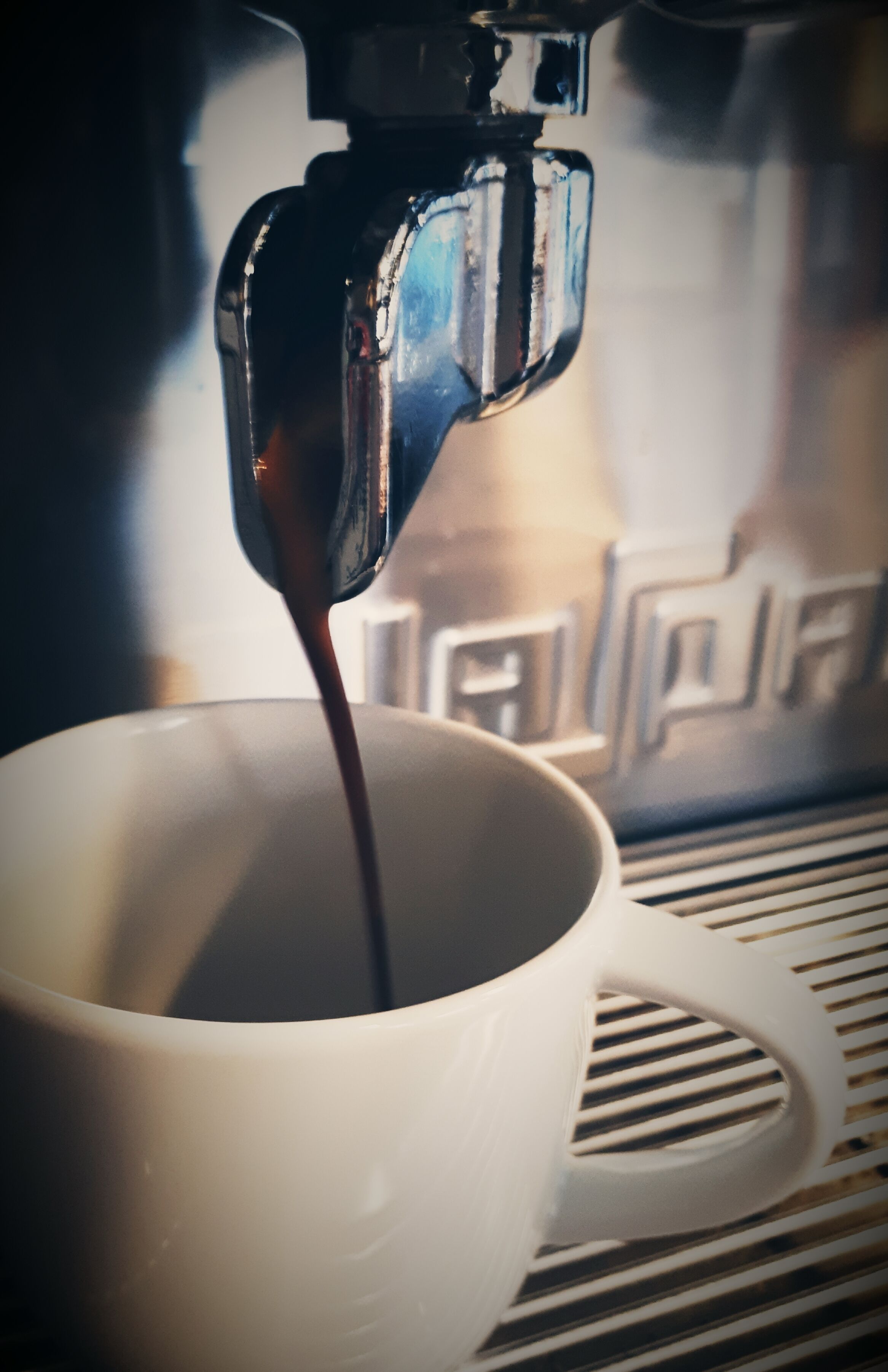 En kaffemaskin som fyller en vit kopp med kaffe.
