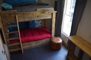 Una cama litera con una escalera, un colchón rojo y un banco de madera.