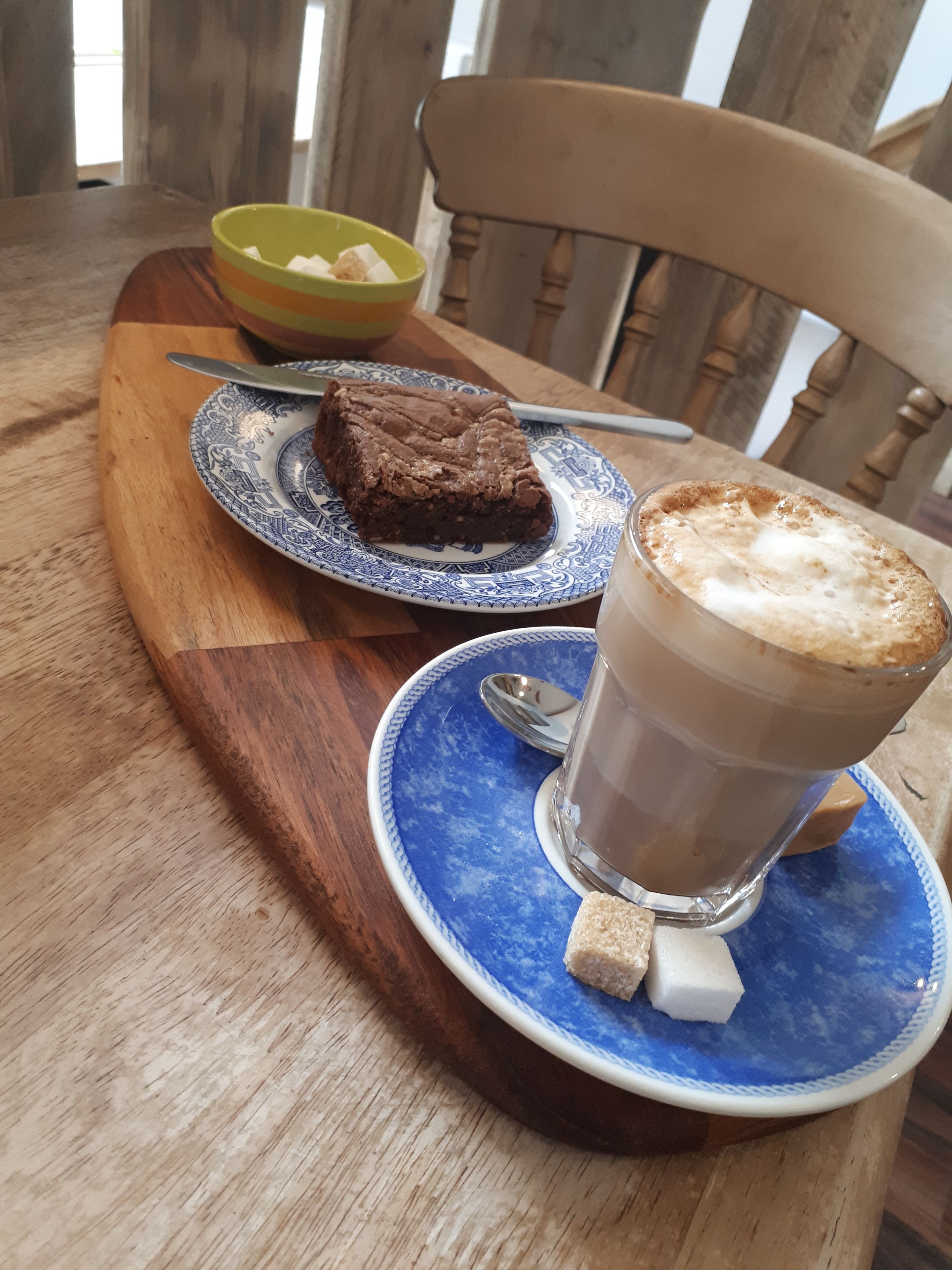 Et træbord med en tallerken brownies, et glas iskaffe og en skål med frugt.