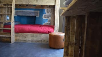A rustic wooden bunk bed with a red mattress and a small round ottoman.
