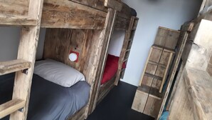 Een slaapkamer met een stapelbed, een houten ladder, een rood kussen en een witte muur.