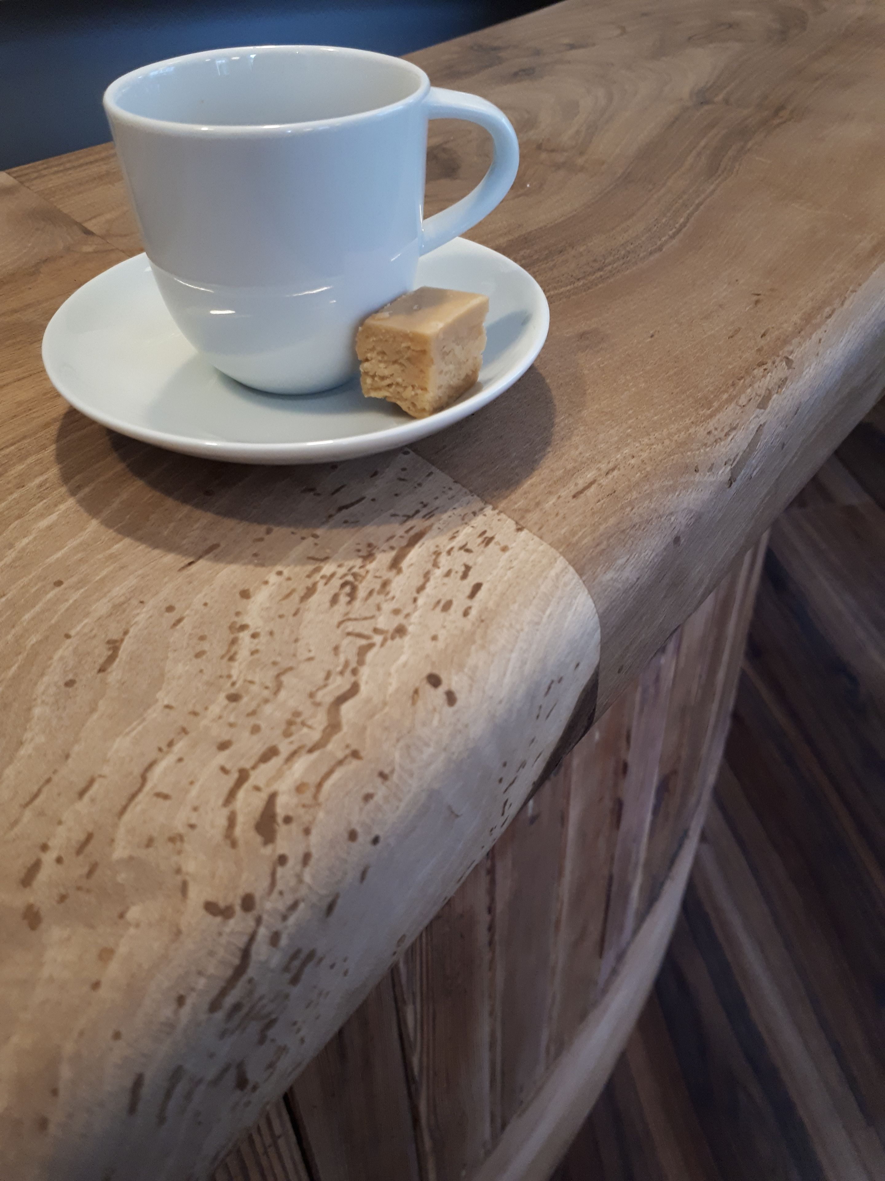 A white cup and saucer with a small piece of food on a wooden table.