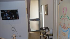 A room with a television mounted on the wall, a dining table with chairs, and a window with curtains. - Bed & Breakfast Il Carignano (Cagliari)