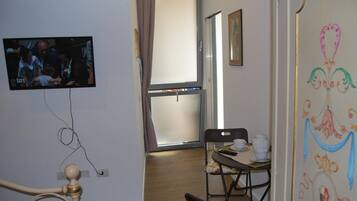 A room with a television mounted on the wall, a dining table with chairs, and a window with curtains.