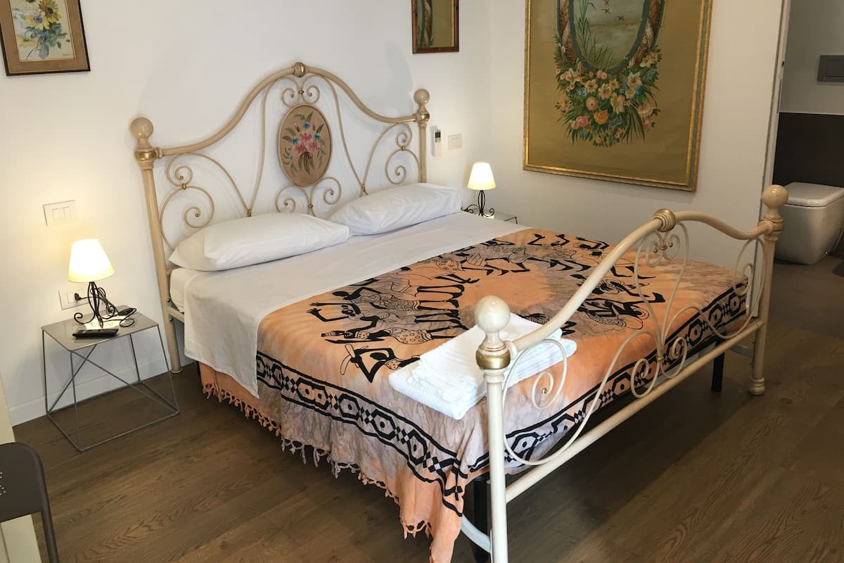 A neatly made bed with a patterned bedspread, a bedside lamp, and a small table with a phone and charger.