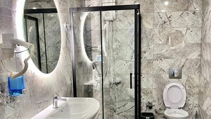 A bathroom with a marble floor, a wooden vanity, a glass-enclosed shower, and a toilet. - Yakamoz Pansiyon (Antalya)