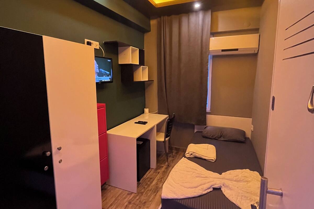 A compact hotel room with a bed, a desk, a chair, a TV, and a wardrobe.
