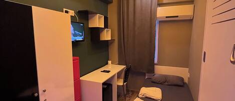 Habitación de hotel pequeña con cama, escritorio, silla, televisor y armario.