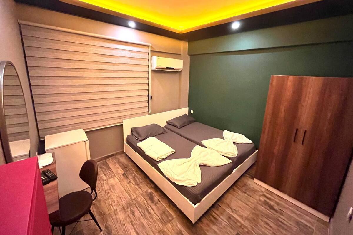 A compact bedroom with a bed, bedside table, chair, wardrobe, and a mirror.