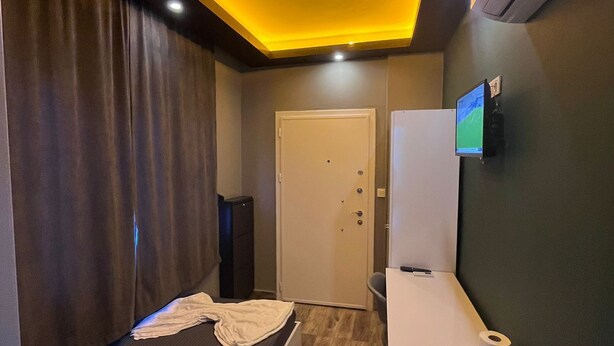 A compact hotel room with a bed, a small desk, a television, and a door. - Yakamoz Pansiyon (Antalya)