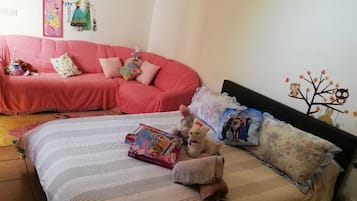 Un dormitorio con cama, un sofá rosa y juguetes infantiles.